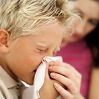 Photo of a boy sneezing into a tissue.